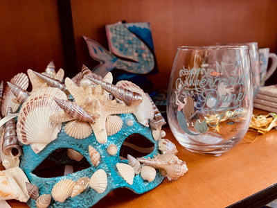 Novelty collections include mermaid gifts, shot glasses, magnets, and local art. Mermaid mask with season shells